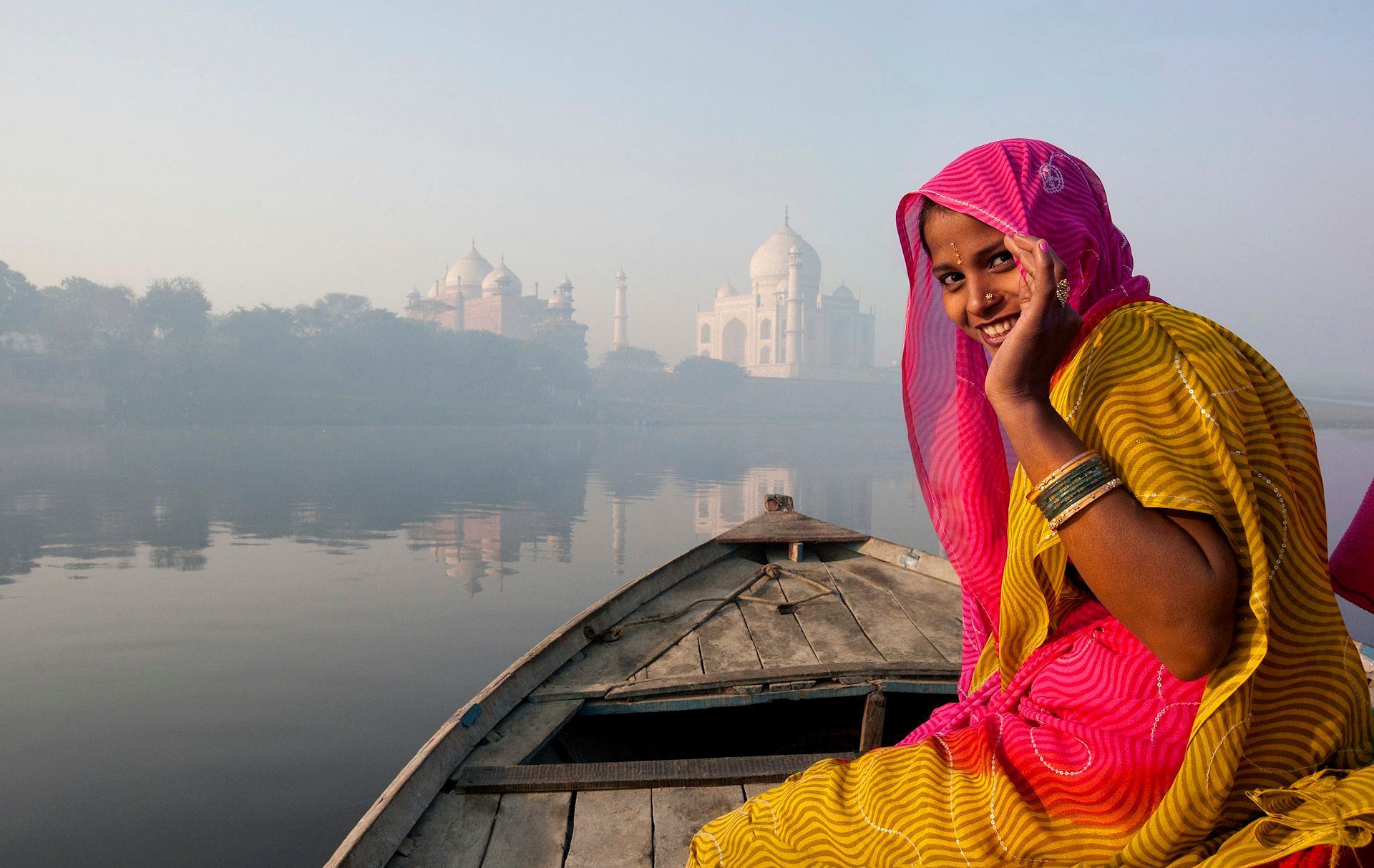 A woman in traditional Indian dress smiles as she rides in a boat towards the epic white marble Taj Mahal