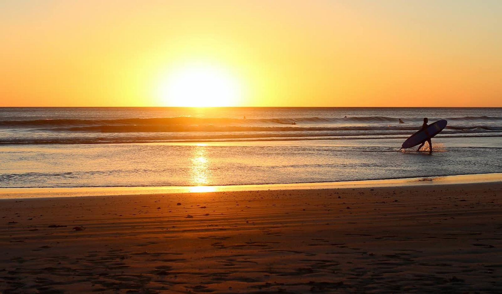 An epic golden sunset on the coast of San Juan del Sur in Nicaragua with a surfer in the distance