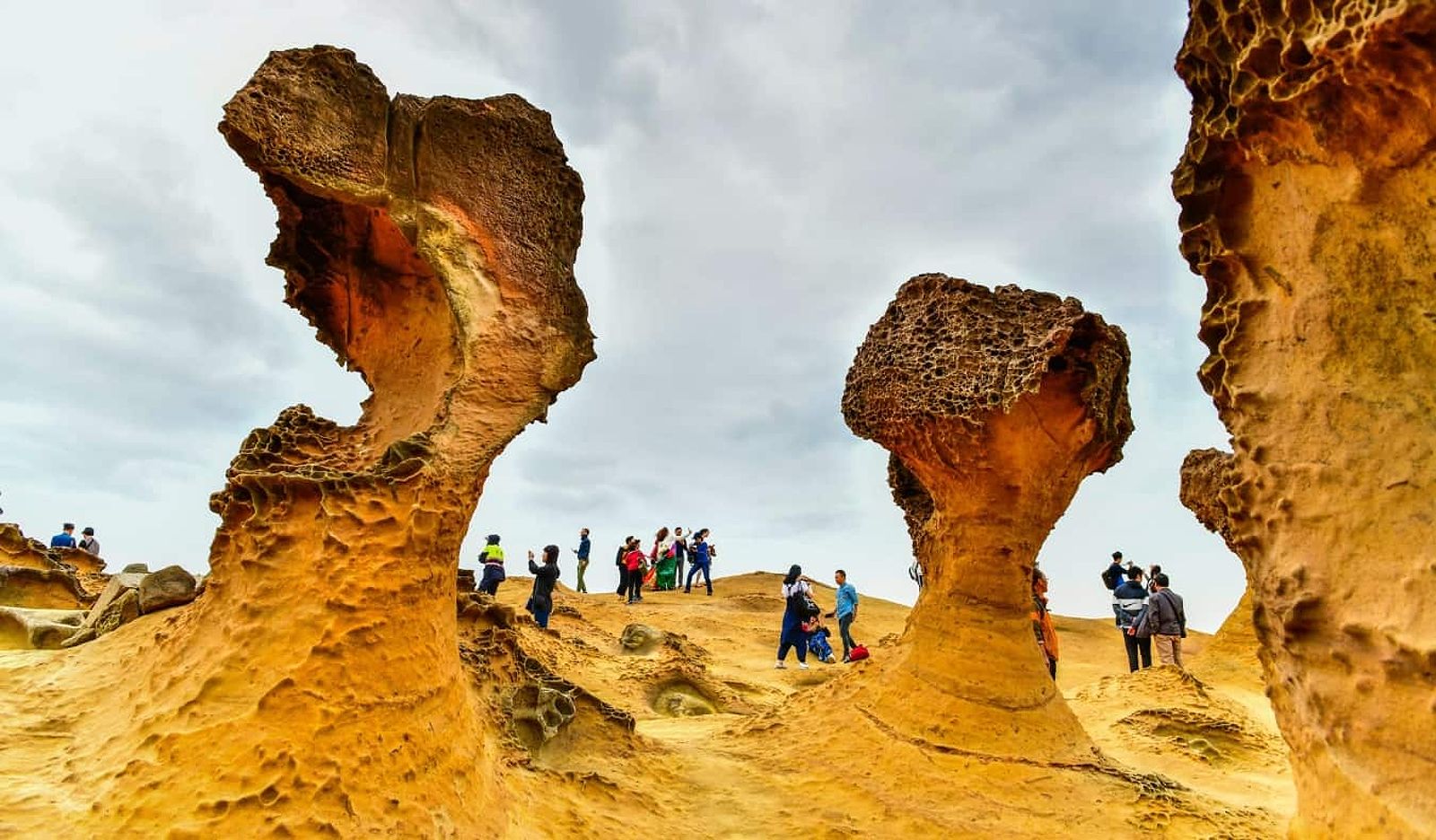 People walking around huge, sandstone colored rock formations in Yehliu Geopark, Taiwan