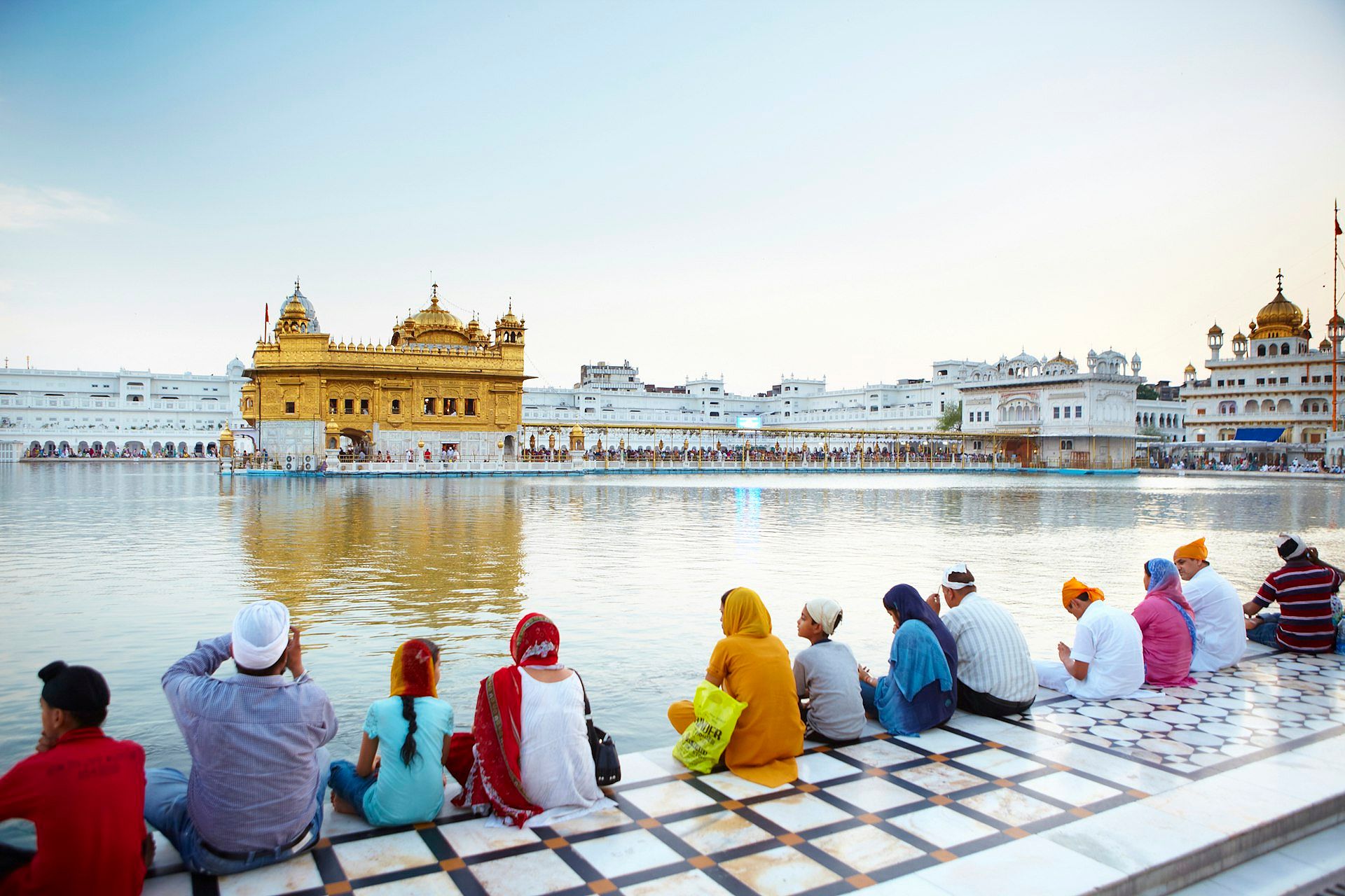 Pilgrims lining walkway across the water from the Golden Temple, a grand square building with a gold facade